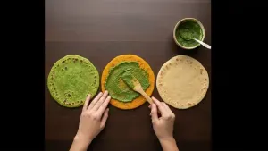 Cooked parathas spread evenly with green chutney using a spoon.