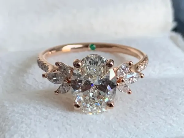 Lab-grown diamond ring from Taylor & Hart with an oval center stone and marquise and round side diamonds on a rose gold band.