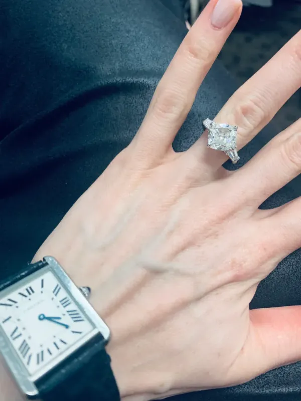 A woman's hand wearing a cushion-cut diamond engagement ring and a Cartier Tank watch.