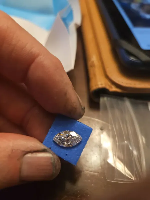 A hand holding a 1.55 carat lab-grown marquise cut diamond on a blue pad.