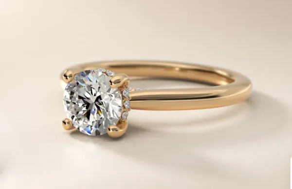 Illustration of a gold engagement ring with a round brilliant diamond in a four-prong setting, with smaller diamonds set along the sides of the basket.