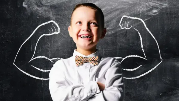 Smiling child standing confidently with crossed arms in front of a chalkboard drawing of muscular arms, symbolizing confidence and inner strength.