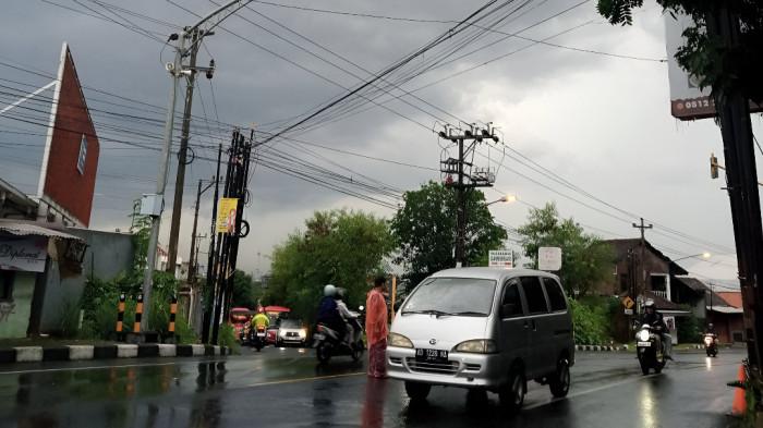 HUJAN RINGAN- Satu kawasan yang berada di Kota Solo dan sekitarnya baru saja dilanda hujan ringan. Seorang pria mengenakan mantel terlihat mengatur lalu lintas.