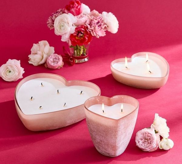 This may contain: two heart shaped candles sitting next to each other on a pink surface with flowers in the background