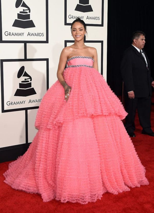 This may contain: a woman in a pink dress on the red carpet at an awards event with people standing around