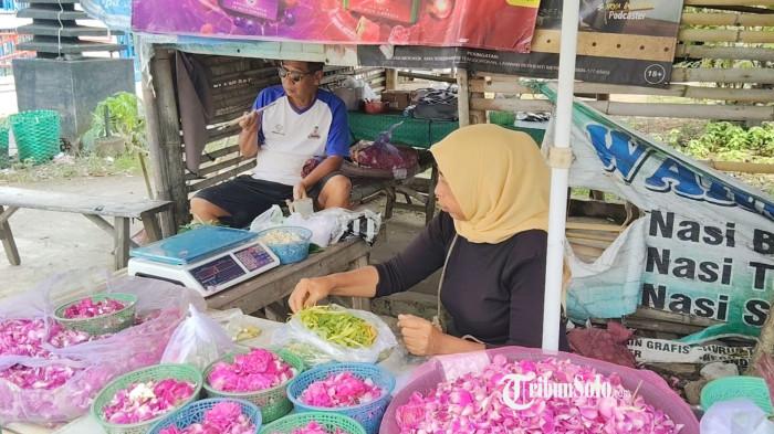 LARIS MANIS - Tjahjadi Widyawati (55) alias Ipung, saat menata dagangannya yakni bunga tabur di lapaknya di Tasikmadu, Karanganyar, Kamis (5/2/2026). Meski permintaan meningkat, Ipung menghadapi kenyataan bahwa harga bunga dari pemasok juga naik dua kali lipat.