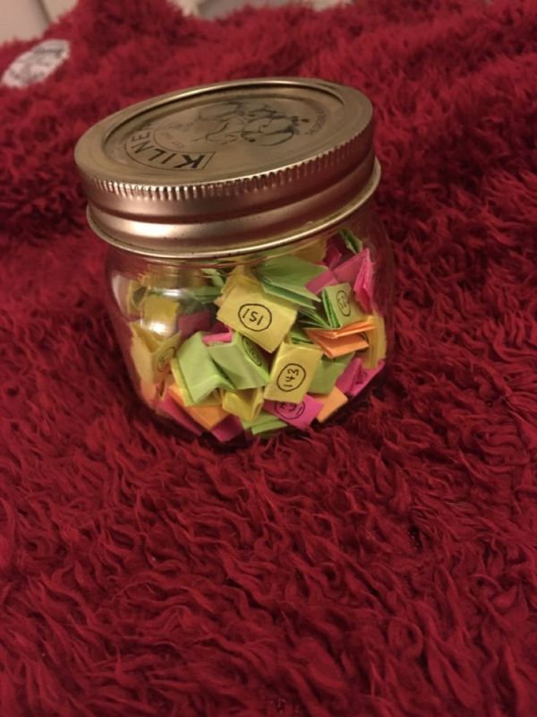 This may contain: a jar filled with lots of colorful origami on top of a red blanket