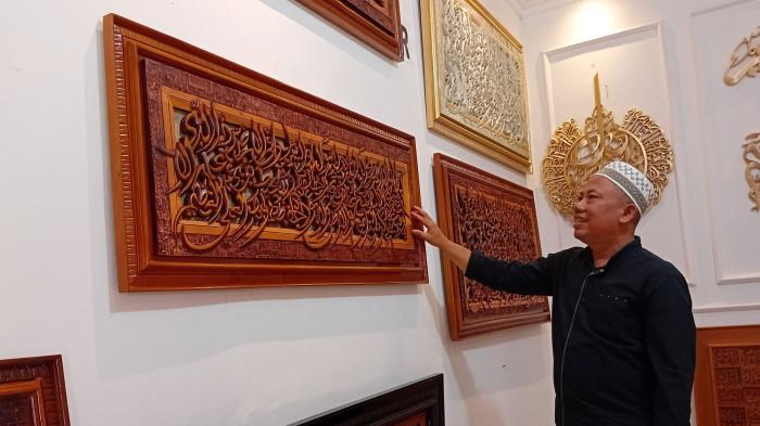 TUNJUKKAN KARYA - Noor Hadi, perajin ukir kaligrafi Desa Pedosawalan RT 09 RW 03, Kecamatan Kalinyamatan, Kabupaten Jepara menunjukkan hasil karya terbaiknya yang dipajang di rumah produksi, Minggu (8/2/2026). Karya ukir kaligrafi produk Nur Art Kaligrafi Jepara kini sudah tembus ke panggung dunia. 