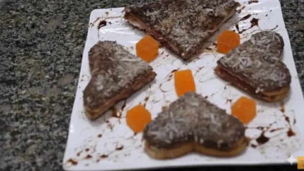 Heart-shaped chocolate lamingtons arranged on a white plate, topped with coconut.