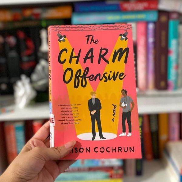 This may contain: a person holding up a book in front of a bookshelf