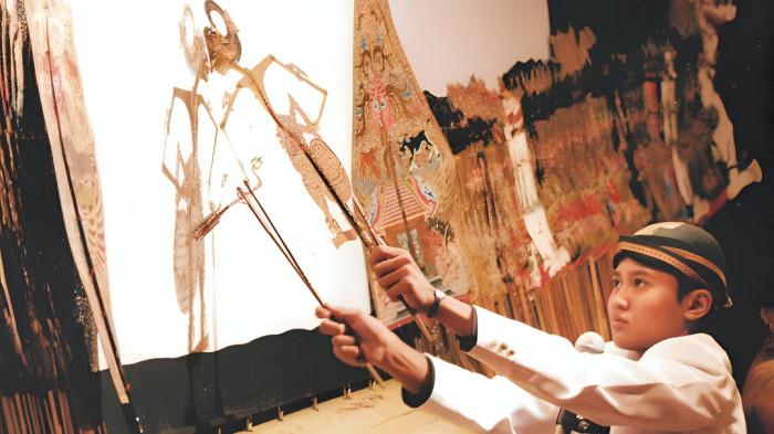 DALANG CILIK- Foto ikonik yang menunjukkan seorang dalang cilik sedang memainkan wayang kulit dalam sebuah pertunjukan seni.