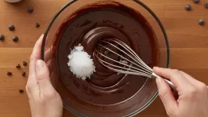 Whisk mixing melted chocolate with sea salt in bowl.