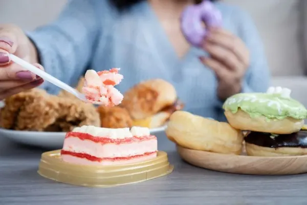 Woman eating too much fast food like burgers, fried chicken, donuts, and sweets, showing signs of binge eating and emotional stress with unhealthy food habits