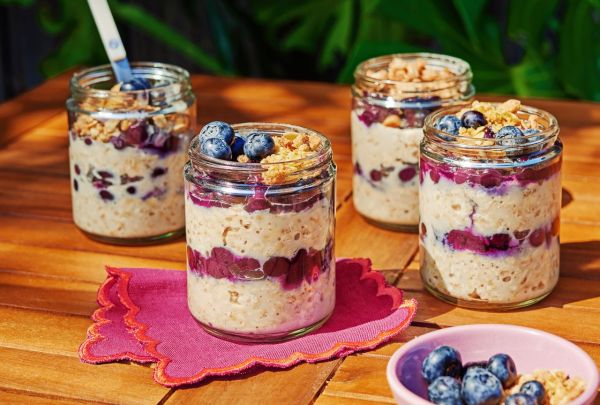 Jars of overnight oats topped with blueberries and granola on a wooden outdoor table Credit: Ali Redmond