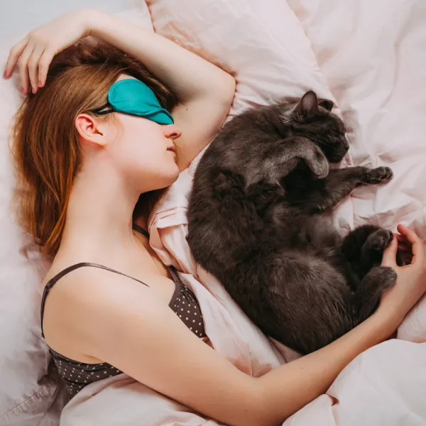 cat keeping sleeping woman warm in bed
