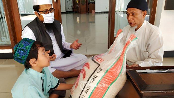 BAYAR ZAKAT- Seorang pria bersama anaknya tengah membayar zakat fitrah yang diterima oleh panita zakat.