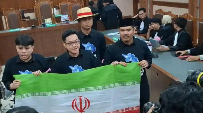 BEBAS - Delpedro Marhaen, Syahdan Husein, Muzzafar Salim, dan Khariq Anhar, membentangkan bendera Iran di ruang sidang Pengadilan Negeri Jakarta Pusat, Jumat (6/3/2026).Mereka akhirnya divonis bebas.