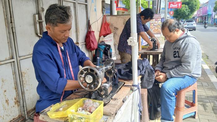 PENJAHIT JALANAN - Sejumlah penjahit di tepi Jalan Jenderal Suprapto Purwokerto, Kabupaten Banyumas, merampungkan pesanan konsumen, Jumat (6/3/2026). Keberadaan penjahit jalanan tersebut ada sejak 23 tahun lalu.