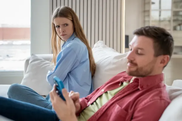 A husband on his phone ignores his angry wife sitting next to him.