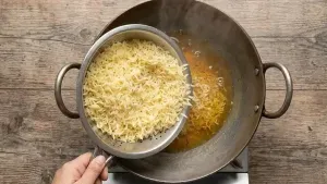 Adding the cooled boiled rice into the prepared sugar syrup and gently mixing so the rice grains do not break.