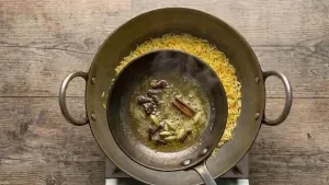 Heating ghee in a small pan and adding cloves, cardamom, and cinnamon to prepare a fragrant tempering.