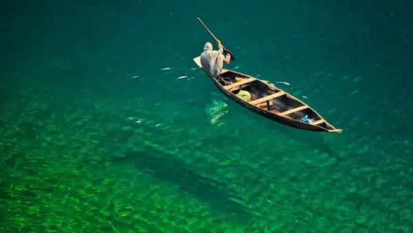 A person in a wooden boat on crystal-clear green water.