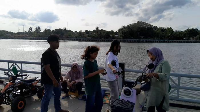 PANEN REZEKI - (Ujung Kiri) Bujang (23) penyedia jasa sewa odong-odong listrik saat sedang melayani pelanggan di kawasan Situ Kulong Minyak, Manggar, Belitung Timur, Selasa (24/3/2026). Di momen libur H+3 Lebaran ini, Bujang mengaku mendapatkan lonjakan pendapatan bak jackpot, dimana dua hari kebelakang ia melayani berpuluh-puluh penyewa jasa hiburan miliknya.