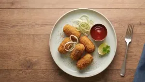 Arrange the croquettes on a plate, garnish with cabbage and cucumber strips, and serve hot with tomato ketchup.