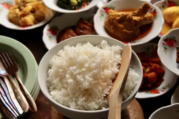 A bowl of steamed white rice in a Padang eatery. The cooked rice is served in a big bowl that serves several portion for a group of diners. In the background is Padang side dishes that accompanies the rice.