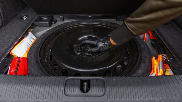 A person taking a spare tire out of a car's trunk