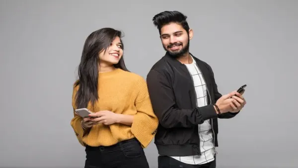 Young man and woman holding smartphones, smiling and looking at each other.