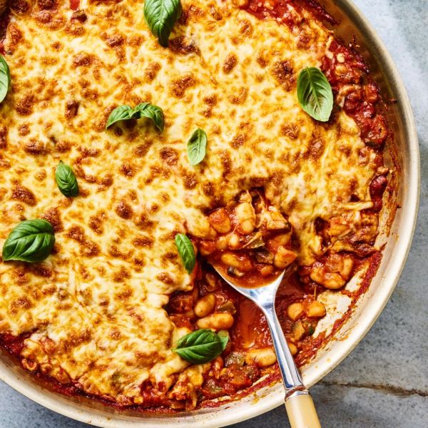 Cheesy baked skillet dish with tomato sauce beans and basil garnish with a serving spoon Credit: Photographer: Morgan Hunt Ward, Prop Stylist: Abby Armstrong, Food Stylist: Ruth Skipworth.