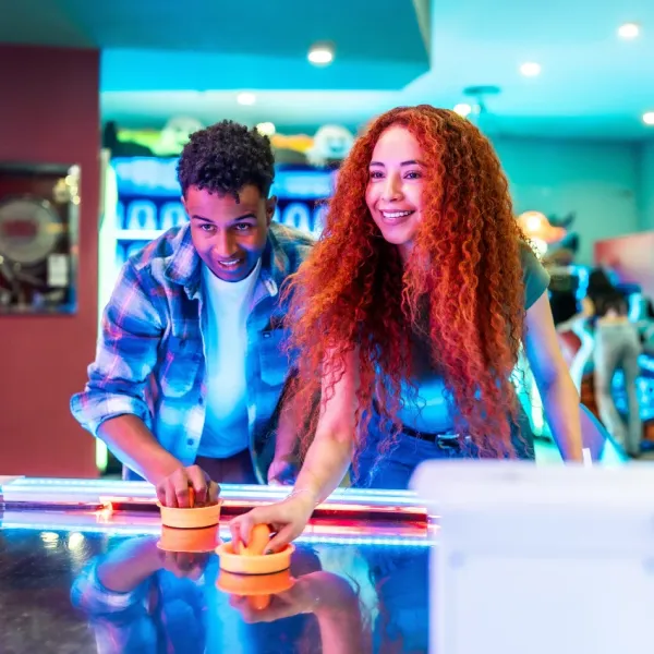 male and female friends playing air hockey at arcade