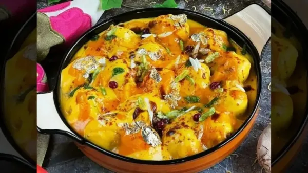 Bowl of mango dahi vada topped with mango yogurt, pomegranate seeds, nuts, and edible silver leaf.