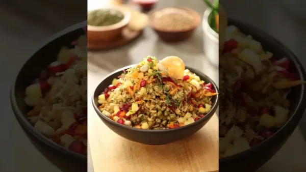 Bowl of healthy sprouts bhel topped with pomegranate, sev, chopped veggies, and spices on a wooden board.