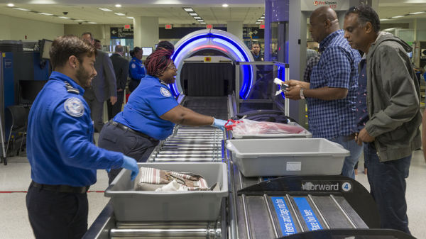 Transportation Security Administration (TSA) agents assist passengers with their bags as they go through a 3-D scanner at the Miami International Airport.