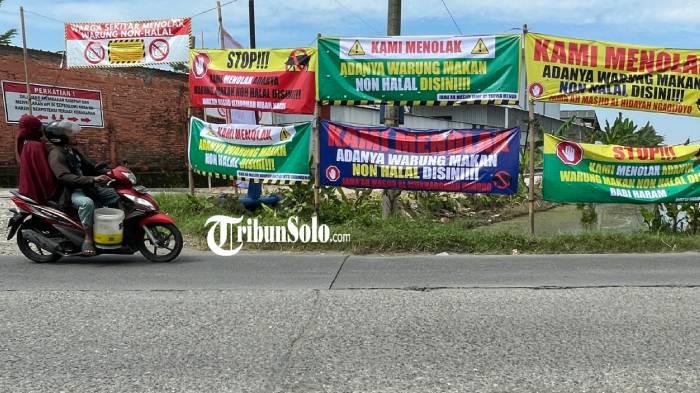 TOLAK. Sebanyak 20 spanduk penolakan terhadap keberadaan kuliner non halal terpajang di sepanjang Jalan Setya Dharma, Dukuh Sudimoro, Desa Parangjoro, Kecamatan Grogol, Kabupaten Sukoharjo, Senin (20/4/2026). Satpol PP sudah pernah melakukan sidak ke lokasi tersebut.