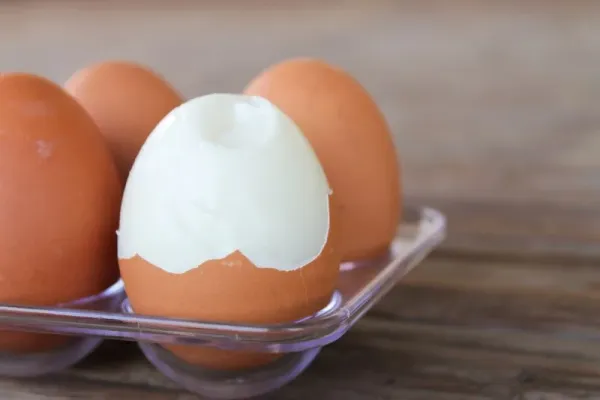 close up Six brown eggs in plastic box on bamboo table with one broken boiled egg.