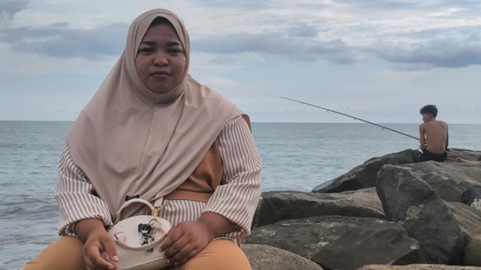 PENCARIAN KORBAN HILANG - Warga sekitar, Sri Puji Astuti saat ditemui di atas batu Pantai Ujung Karang, Kecamatan Padang Utara, Kota Padang, Sabtu (24/4/2026) kemarin. Sri sebut plang tersebut berfungsi sebagai pengingat bagi pengunjung, karena larangan dari masyarakat tidak efektif.