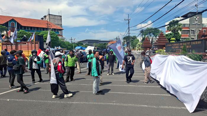 UNJUK RASA - Massa yang tergabung dalam aliansi Driver Online Bubarkan Aplikator Nakal (Dobrak) Jatim, menggelar unjuk rasa di depan Gedung DPRD Jawa Timur, Surabaya, Selasa (28/4/2026) sekitar jam 12.00 WIB. Mereka menuntut anggota dewan segera menyusun peraturan daerah, soal penentuan tarif ojek online