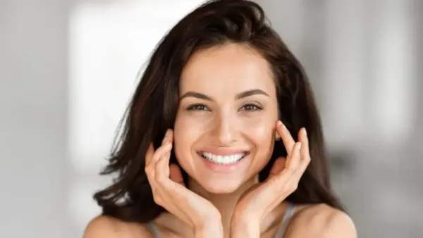Smiling woman with clear, radiant skin gently touching her face.