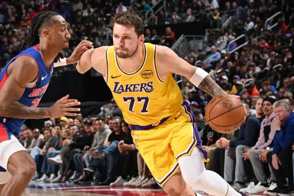 Luka Doncic in a yellow Lakers jersey dribbles past a Detroit Pistons player.