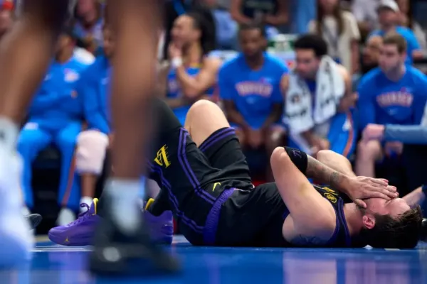 Luka Dončić lies on the court holding his face in his hands during a basketball game.