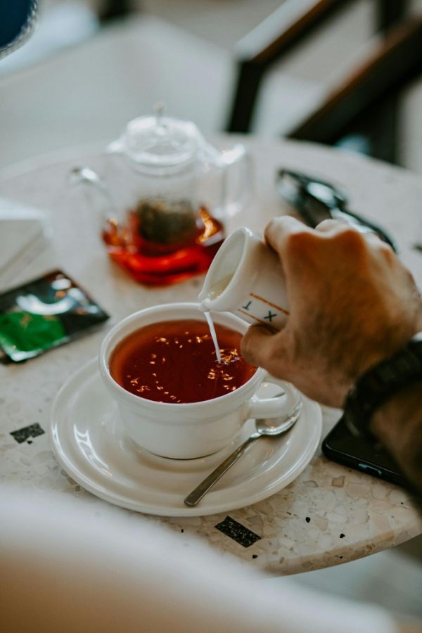A hand pouring milk into tea. Photo by Pexels