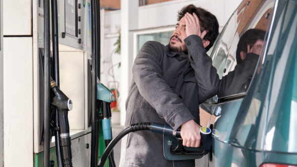 A worried-looking man pumping gas into a green minivan