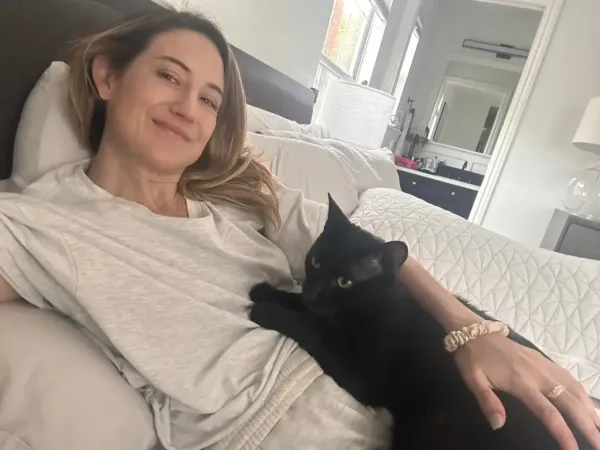 Lindsey Hall smiles in bed with a black cat on her lap.