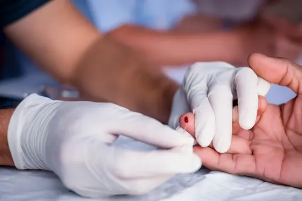 A healthcare professional in white gloves performing a fingerstick blood draw for a hematology test.