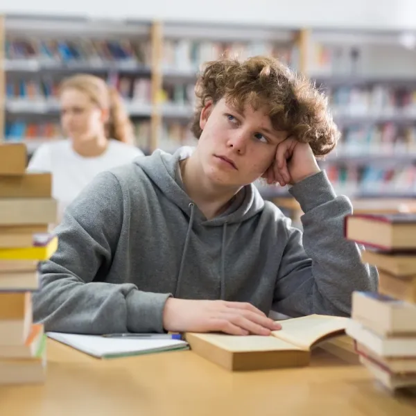 bored teenage male student with book in library hasn't learned accountability