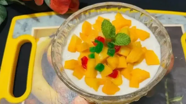 Delicious mango pudding topped with fresh fruit chunks, colorful tutti frutti, and mint leaves in a crystal bowl.