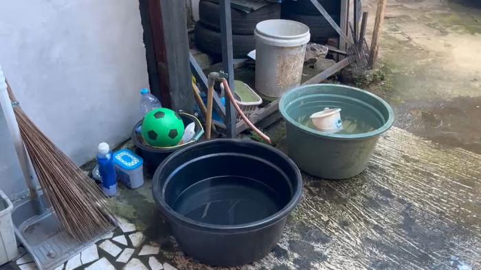 PDAM TIDAK NGALIR - Nurhikmah saat menadah air hujan di teras rumah pakai baskom di Keluruhan Rimuku, Kecamatan Mamuju, Kabupaten Mamuju, Selasa (19/5/2026).